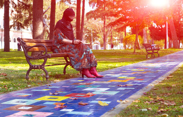 Wall Mural - Eastern Woman sitting on bench at colourful Park Alley