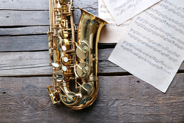 Wall Mural - Beautiful golden saxophone with musical notes on wooden background, close up