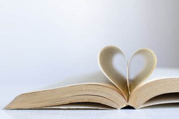 Open old book on a table with pages in a heart shape and neutral background