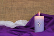 Purple Easter candle by fabric, white cloth and burlap blurred in background