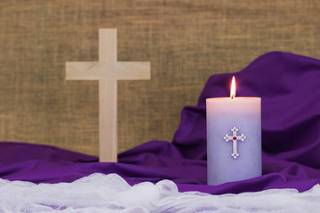 Purple Easter candle burning with fabric and blurred wooden cross in background