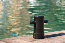Black Mooring Bollard / Detail Of Old And Black Mooring Bollard On The Wooden Pier With Water In The Background