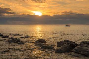 Wall Mural - Dramatic sunset at the ocean with boulder rocks and fishing boat