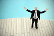 © Westend61 - Barefoot businessman wearing black suit standing in front of swimming pool with arms raised