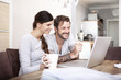 © Westend61 - Smiling couple sitting at wooden table looking at laptop