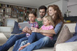© Westend61 - Couple sitting with their with two little daughters on couch in the living room looking at digital tablet