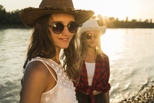 Two Friends Wearing Straw Hats And Sunglasses At The Riverside At Sunset