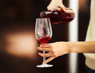 Wall Mural - Young woman pouring pink wine into glass on blurred background