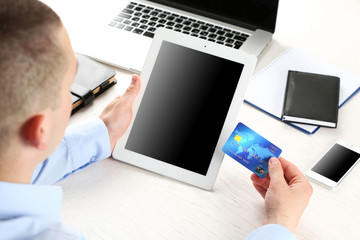 Wall Mural - Man holding credit card and tablet on workplace background