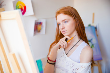 Canvas Print - Thoughtful pretty young redhead woman artist thinking and making sketches