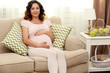 © Africa Studio - Cute happy pregnant woman on sofa in the room