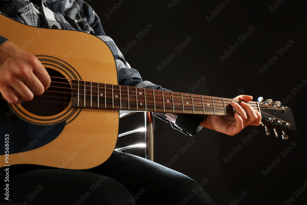 Musician plays guitar on black background, close up