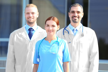 Poster - Happy team of young doctors standing against hospital entrance