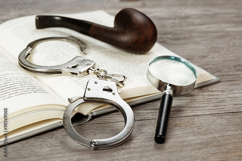 Fotografia handcuffs, magnifying glass and pipe on book