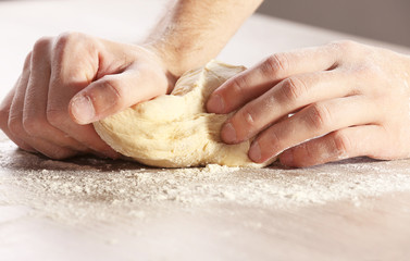 Wall Mural - Hands kneading dough for pizza on the wooden table, close-up