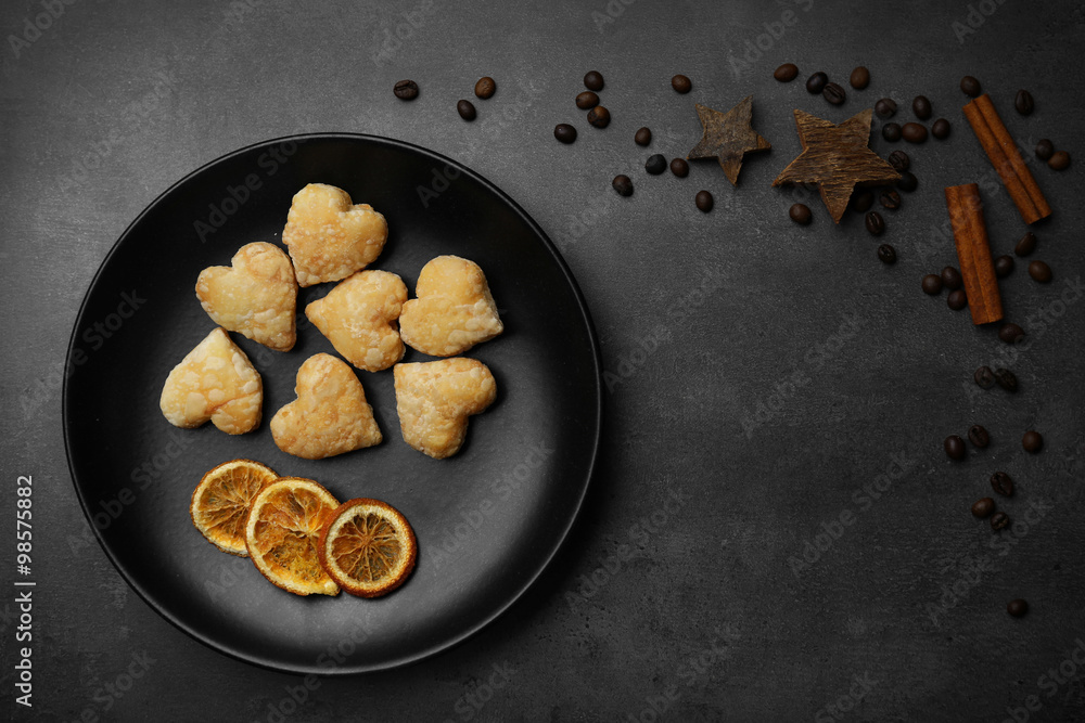 Heart shaped biscuits on pan with dried spices on dark grey background