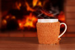 Hot drink in a mug wearing a knitted clothes on the background of the fireplace.
