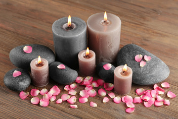 Alight wax grey candle with flower petals and pebbles on wooden background