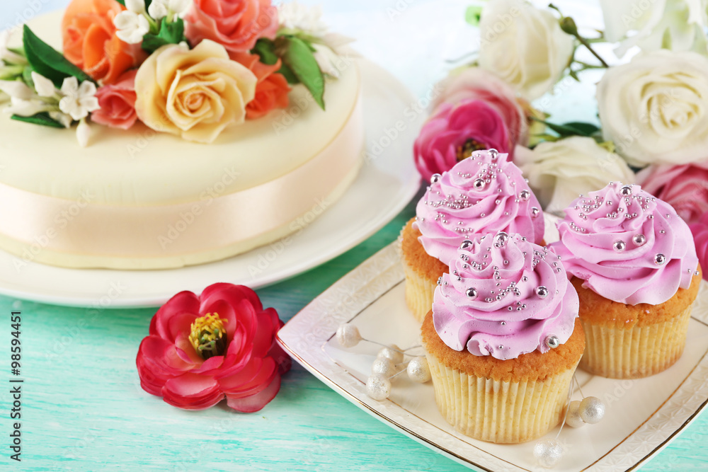 Cake with sugar paste flowers and cupcakes, on light background