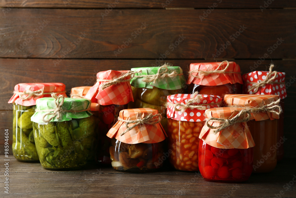 Jars with pickled vegetables and beans on wooden background