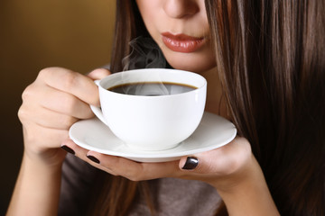  Woman holds cup of coffee and saucer in hands, close up