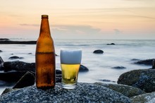 Glass Of Beer And Bottle Of Beer On A Rock On The Beach