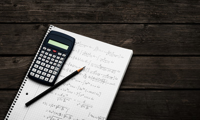 Maths concept - handheld calculator and pencil over a sheet of paper with maths-formulas