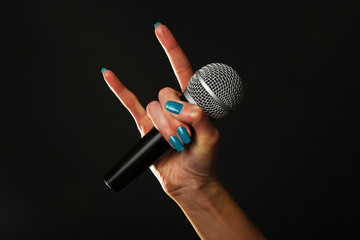 Woman hand with microphone and devil horns isolated on black