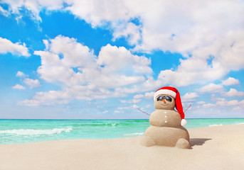 Smiling sandy Snowman in Christmas Santa hat on tropical beach