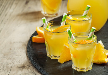 Orange drink in small glasses with striped straws and pitcher, s