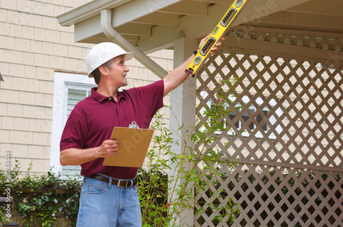 Fotografie, Obraz A home inspector or house building repair contractor in a hard hat holding a lev