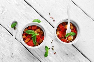 Tasty vegetarian ratatouille made of eggplants, squash, tomatoes in bowls on wooden table background