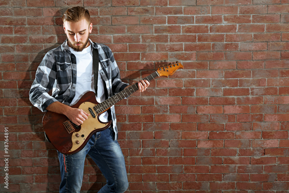 Young man playing guitar on brick wall background