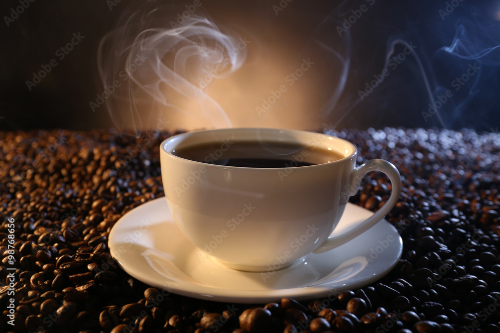 Cup of hot coffee among coffee beans on dark background
