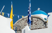 A Greek Orthodox Church With Blue And Yellow Prayer Flags In Oia Town On The Island Of Santorini, Greece
