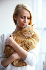 Wall Mural - Young woman holds red cat in hands, close up