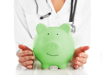 Doctor in white uniform with stethoscope holding green piggy bank isolated on white