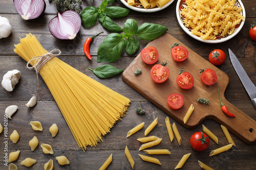 Fotografía Vista dall'alto Pasta grezza con Basilico e Pomodoro su sfondo legno rustico