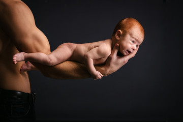 Young Caucasian man holding holding little son over black background