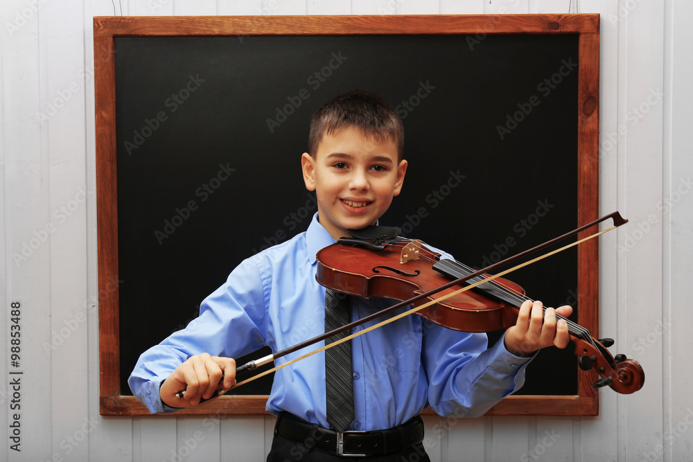 Young cute schoolboy playing the violin at the blackboard