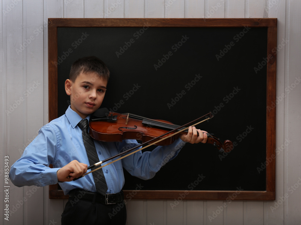 Young cute schoolboy playing the violin at the blackboard