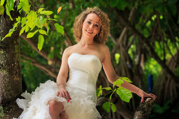 blonde bride in fluffy dress sits on trunk groom stands near