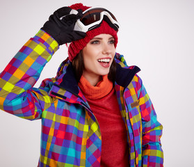 Young smiling woman is posing with ski goggles in studio, isolat