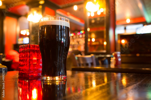 Fotografie, Obraz Glass of dark beer with candle in pub setting