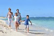 © goodluz - Family of four running on a sandy caribbean beach
