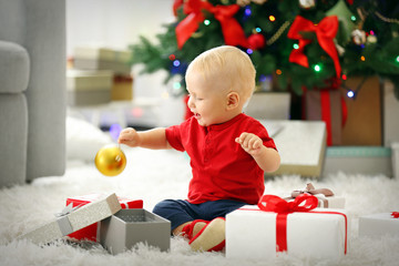 Funny baby with gift boxes and Christmas tree on background