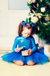 © tenrec - Girl in blue dress sitting near Christmas tree with gifts