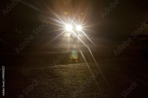 Fényképezés  A shadowy figure standing in front of vehicle headlights in the dark of night