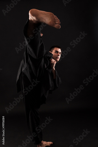 Принти на полотні Studio portrait of young karate fighter kicking over black background