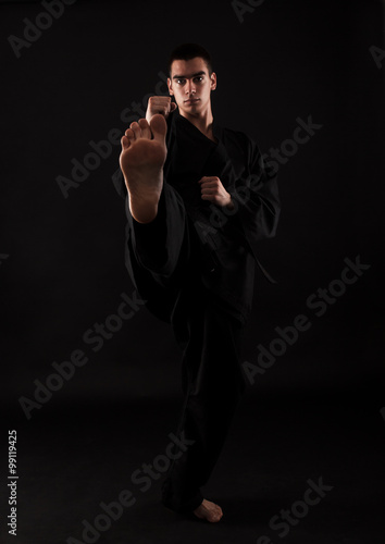 фотографія Studio portrait of young karate fighter kicking over black background